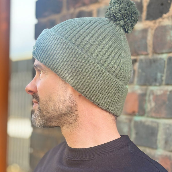 side of man wearing olive green beanie hat with detachable bobble