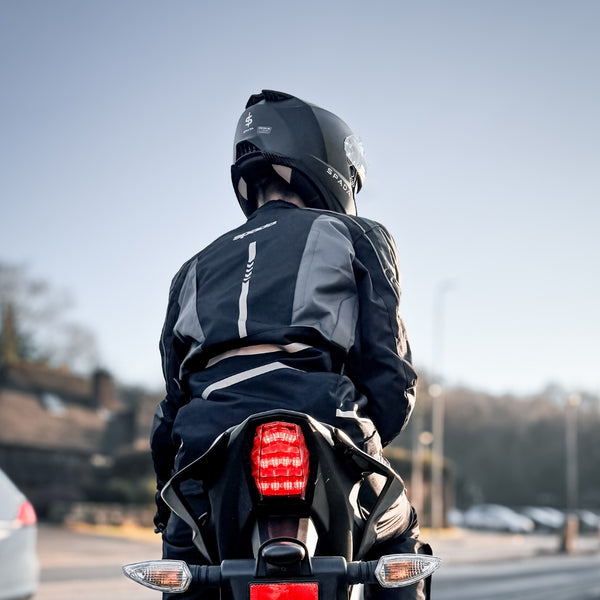 Biker wearing black motorcycle jacket sitting on bike with helmet, showcasing ventilation and protective fit.