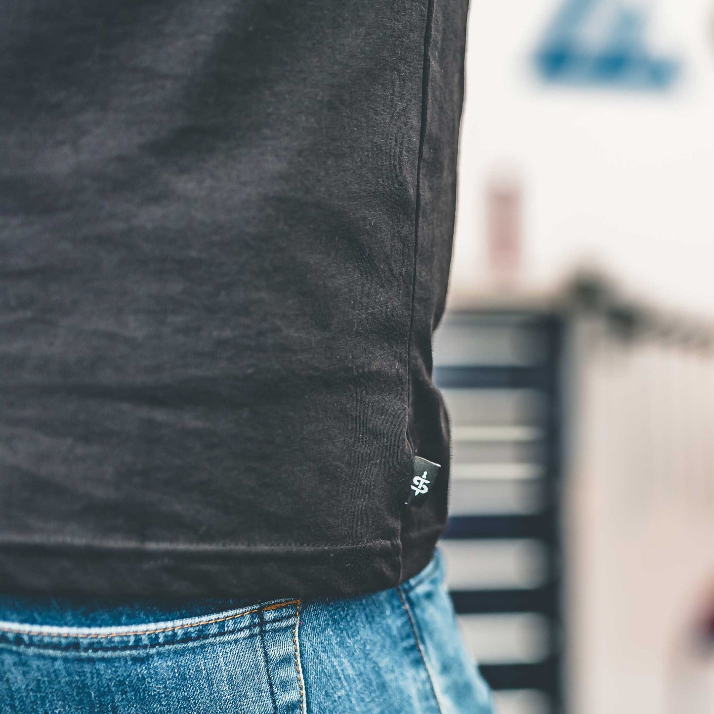Person wearing a dark gray t-shirt with a small logo on the chest, standing outdoors.