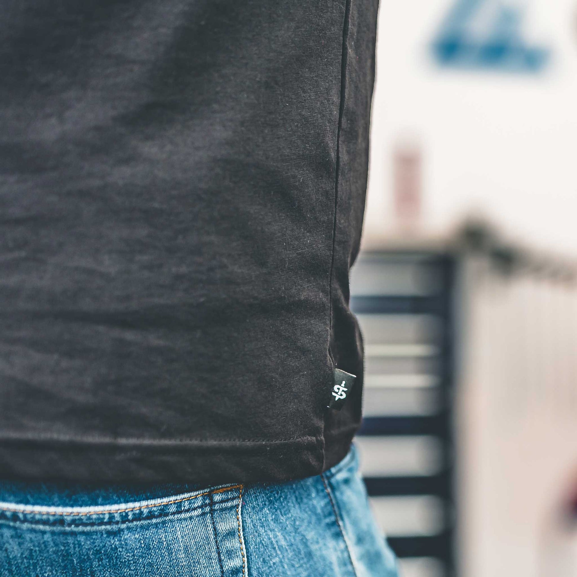 Person wearing a dark gray t-shirt with a small logo on the chest, standing outdoors.