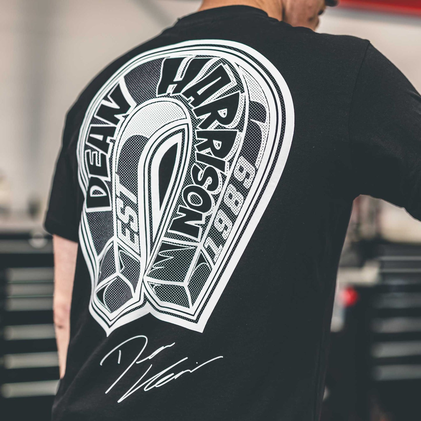 Person wearing a black t-shirt with a white graphic design on the back, set against an indoor background.