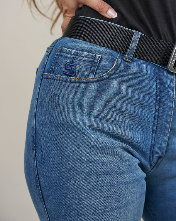 Close-up of blue jeans with a brand logo on the pocket against a neutral background