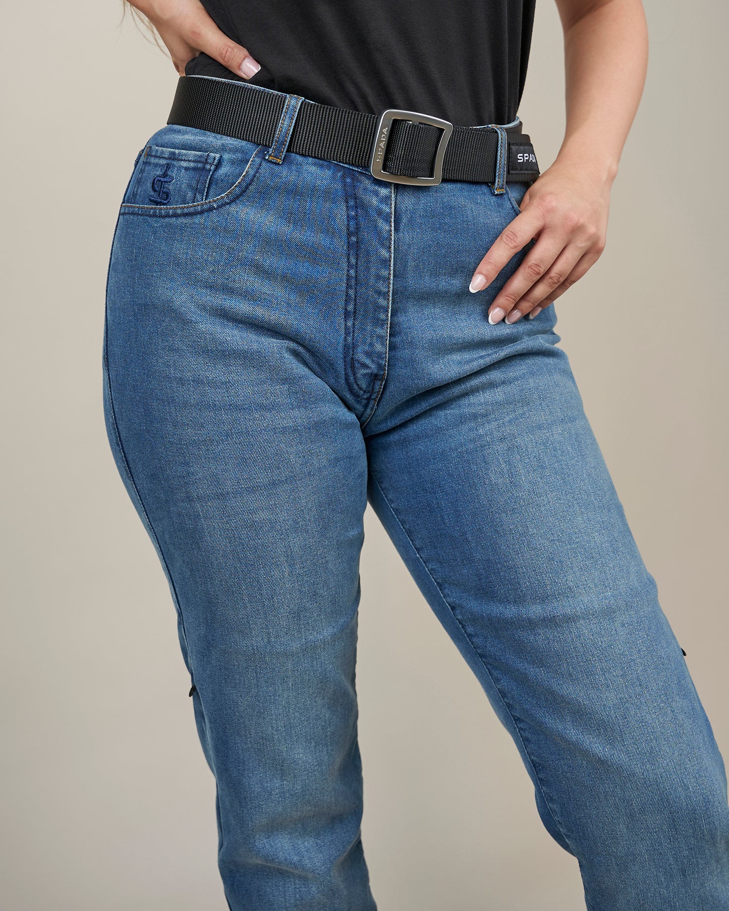 Person wearing blue jeans with a black belt on a neutral background