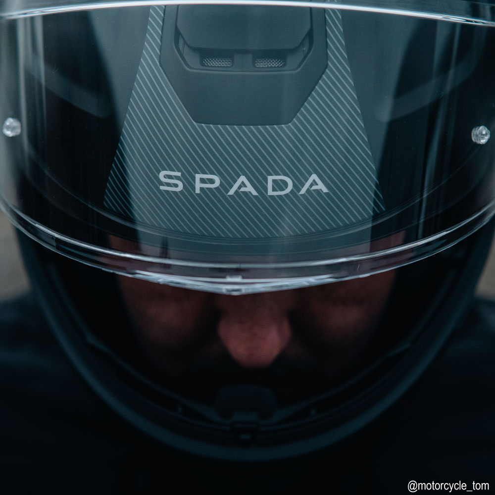 closeup of front of biker wearing motorbike helmet with clear visor and spada logo