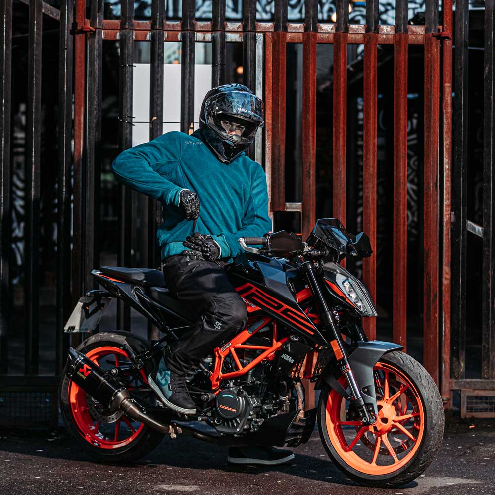 Full body view of male rider in Blade Blue motorcycle hoodie next to orange and black motorbike – street style with biker protection