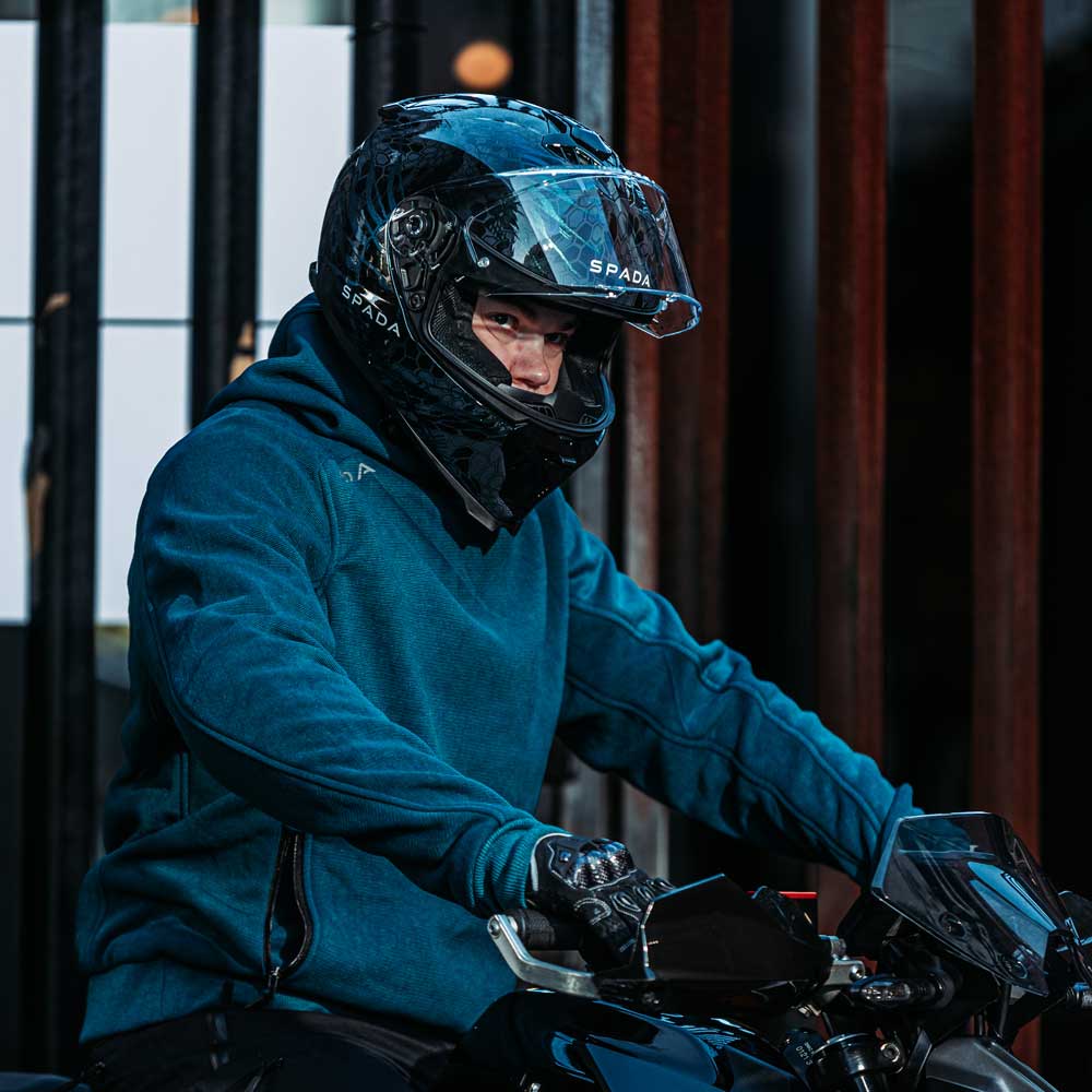 Male biker wearing Blade Blue motorbike hoodie while seated on motorcycle with helmet – casual look, road-ready construction