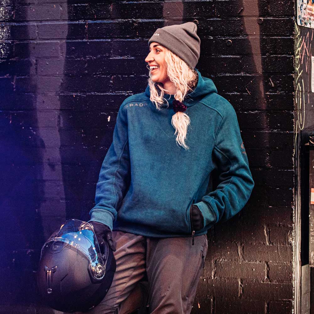 biker girl wearing blue motorcycle hoodie while holding motorbike helmet