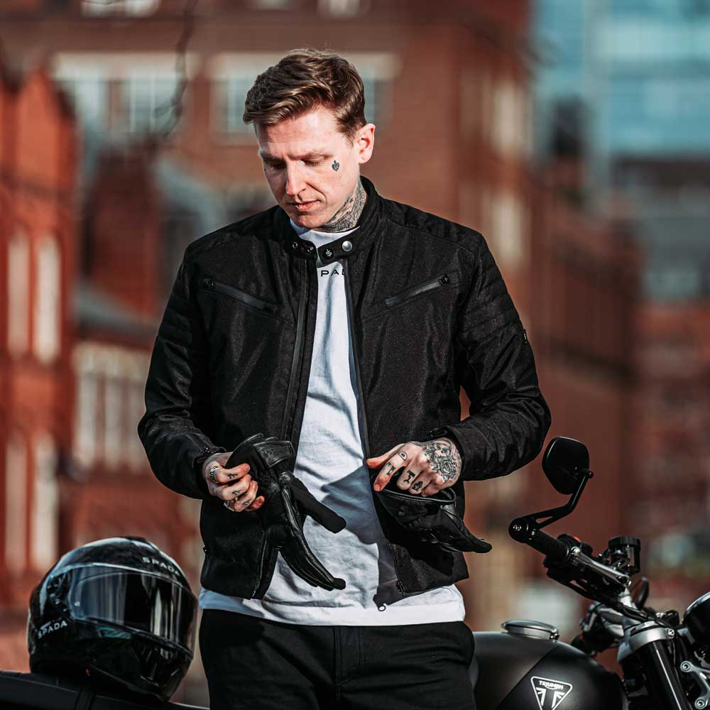 biker wearing black waterproof motorcycle jacket putting on matching black motorcycle gloves