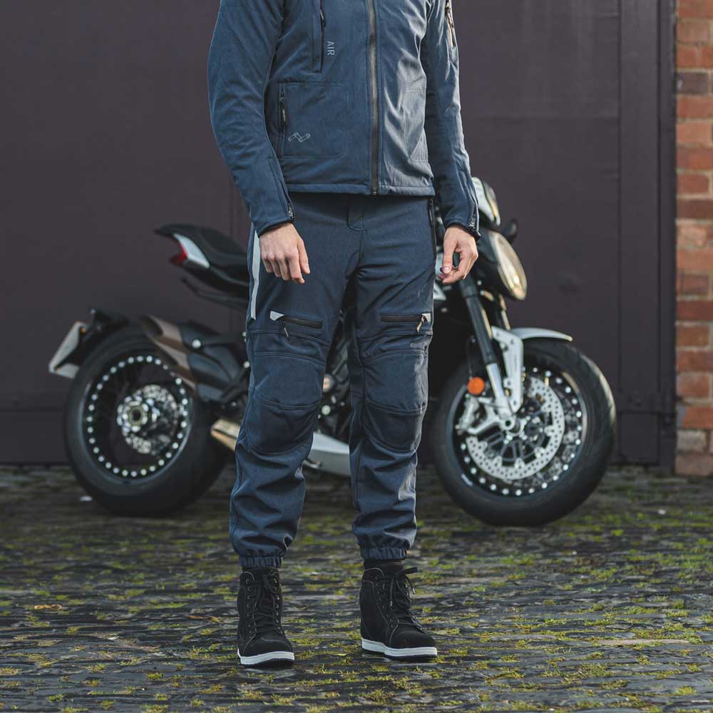 biker wearing blue waterproof motorcycle trousers and matching biker jacket with black trainers