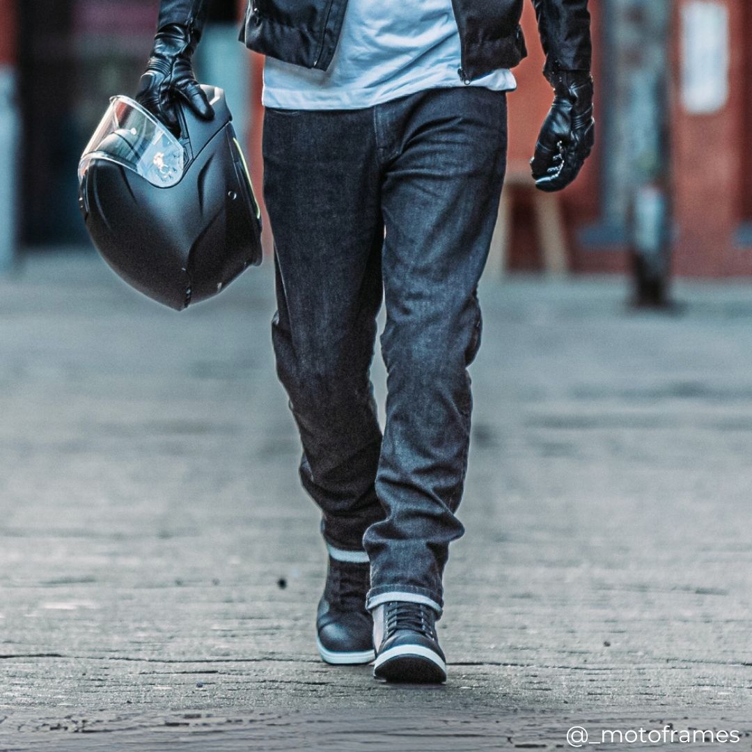 biker walking wearing black motorcycle jeans with black motorbike helmet and gloves