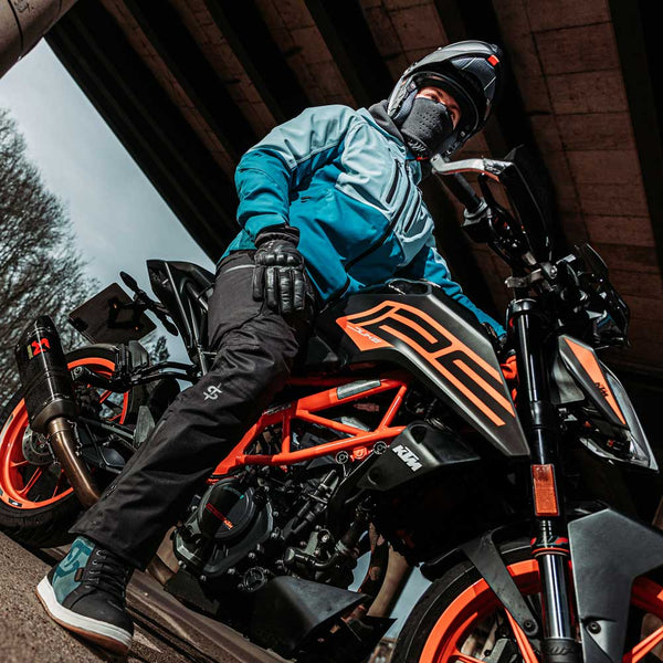 Side view of man in two-tone blue motorbike jacket beside orange and black motorcycle, weatherproof jacket for men who ride