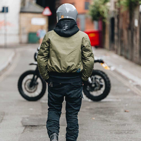 biker walking towards motorbike wearing motorbike gear including green jacket