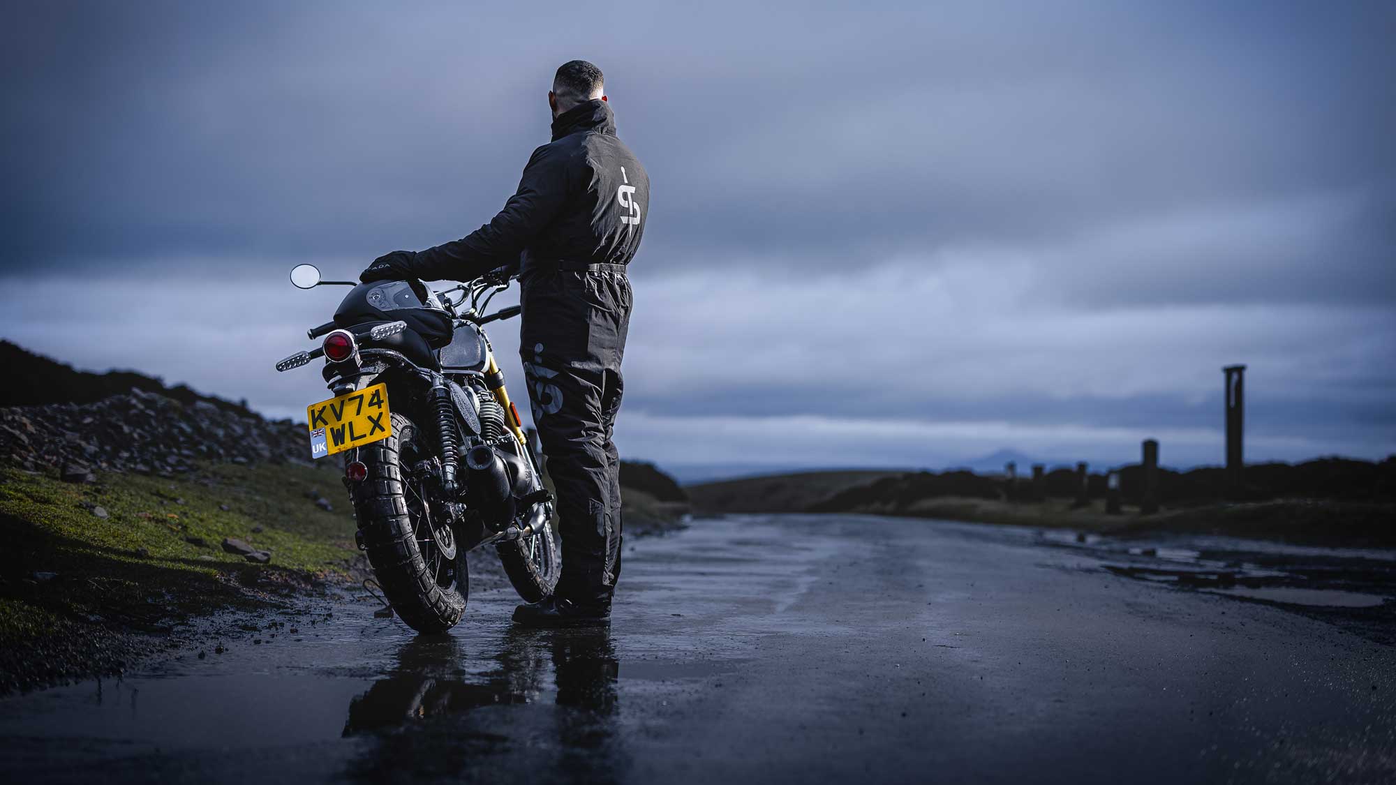 biker with motorbike on open road in nature wearing all black motorcycle gear