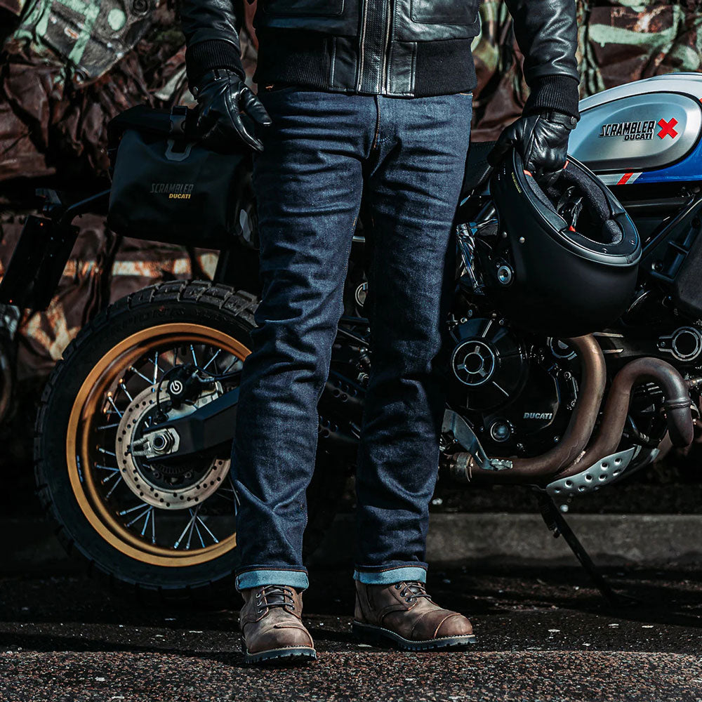 biker wearing spada raw indigo motorcycle jeans riding a motorbike and holding a helmet