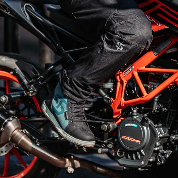 biker wearing black motorcycle trousers and black and blue motorbike trainers on motorbike