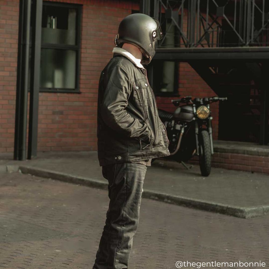 Side profile of biker in Temper Black and Tan Trucker Motorcycle Jacket with riding jeans and helmet – classic trucker design with modern protection.