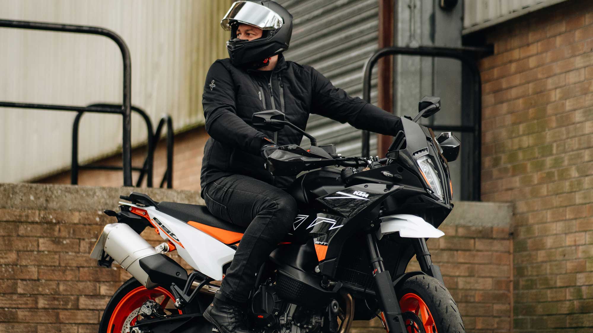 biker wearing black waterproof motorcycle jacket on black and orange motorcycle