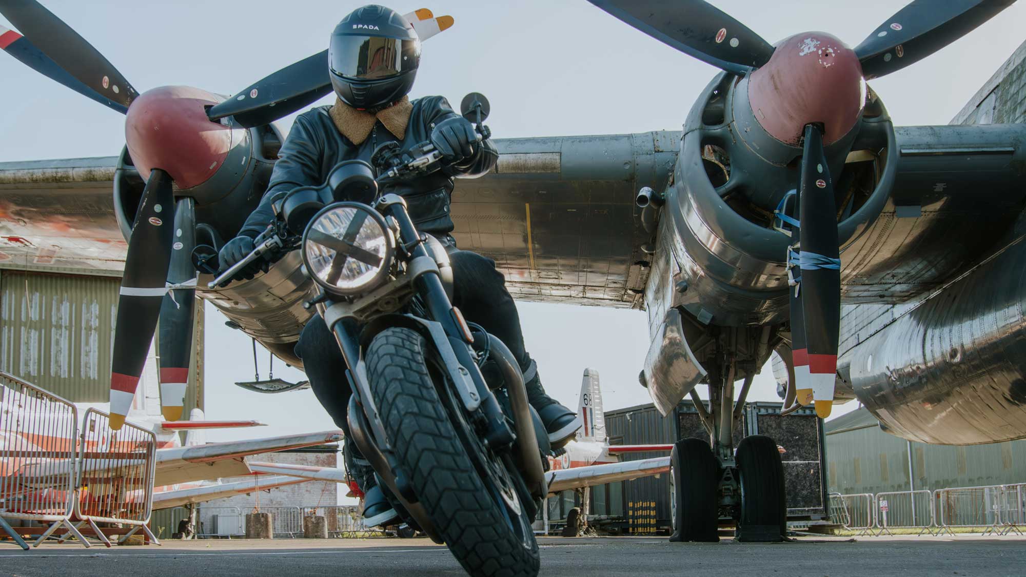 biker wearing black leather jacket and motorbike helmet riding bike with airplanes on enfield