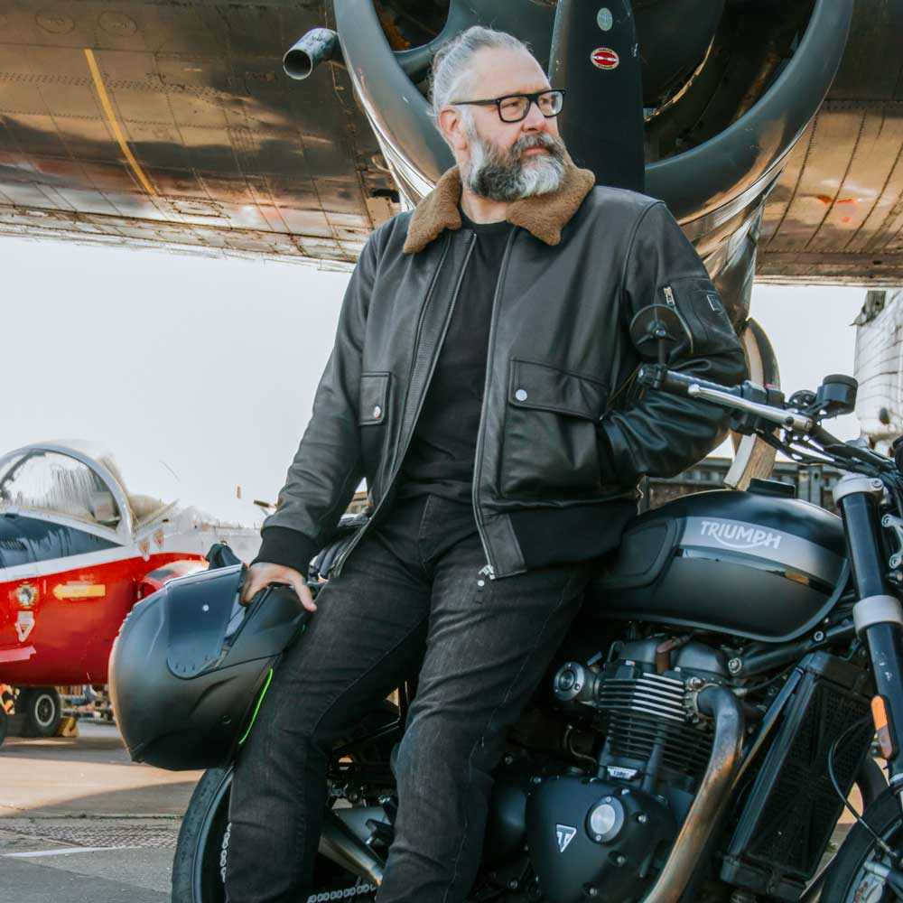 Man wearing Turbine leather jacket unzipped, leaning on motorbike and holding helmet – ready-for-the-road biker look