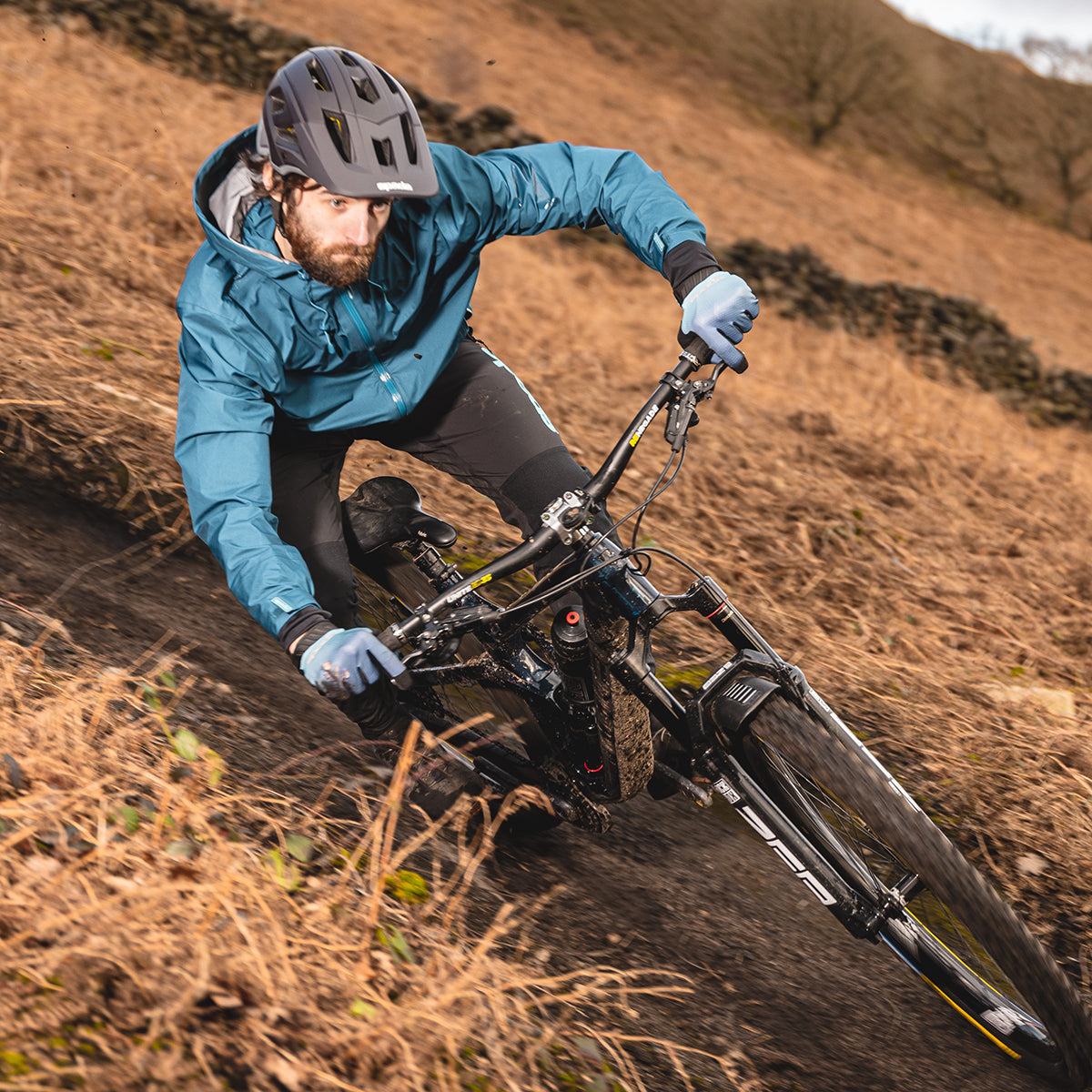 biker riding mountain bike outdoors with blue waterproof jacket and black helmet