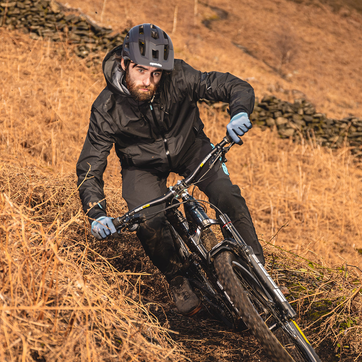 biker riding mountain bike outdoors wearing full black mtb gear