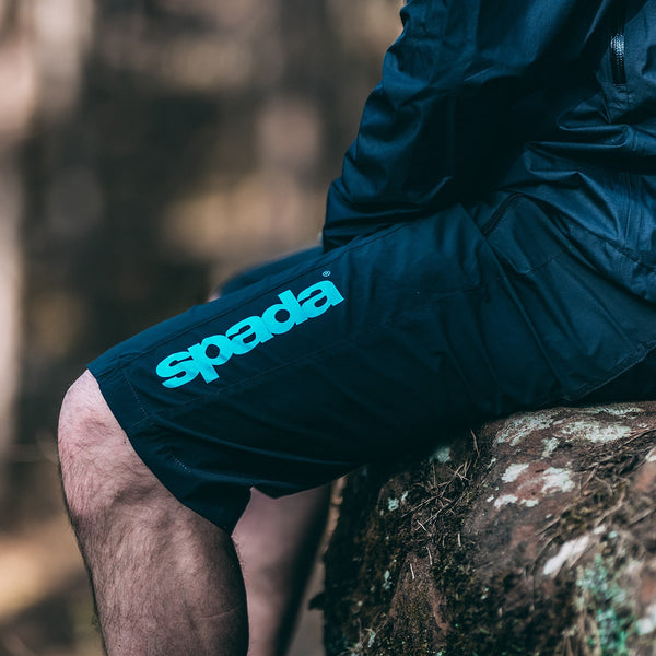 biker sat on a rock outside wearing black biker shorts with blue spada branding