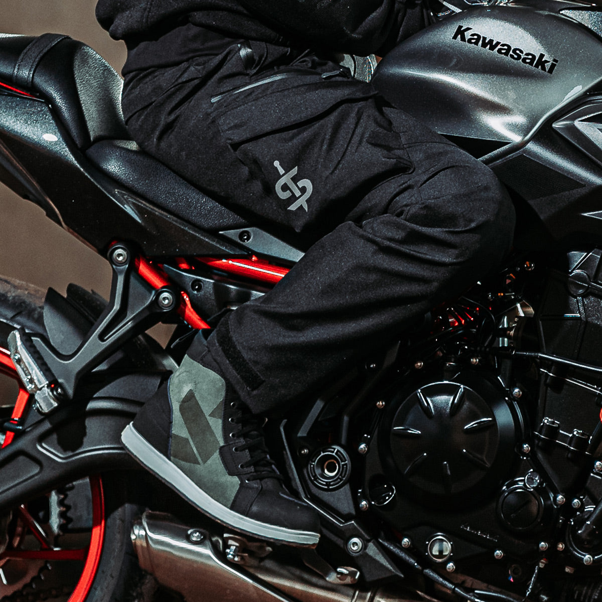 biker riding a kawasaki motorbike wearing black motorcycle trousers with a pair of olive green and black trainers