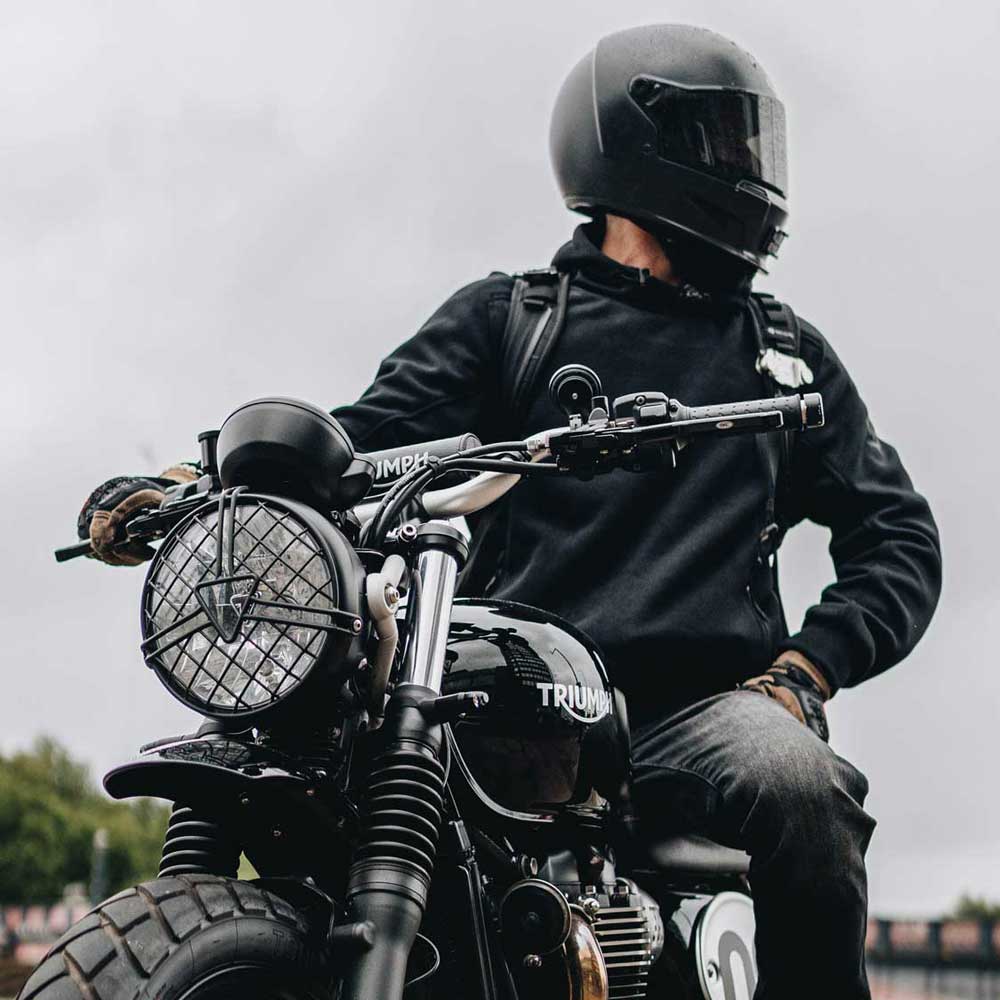 biker wearing black motorcycle hoodie with black motorcycle helmet riding a triumph motorbike