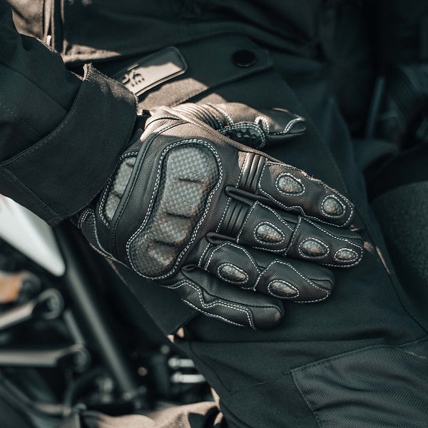 Close-up of black Enforcer Rev 2 motorcycle gloves held by a person wearing Nodachi Motorcycle Jacket and trousers.