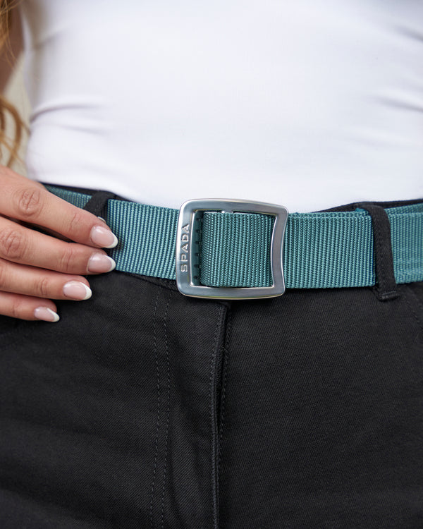 Person wearing a teal belt with a silver buckle on black pants.