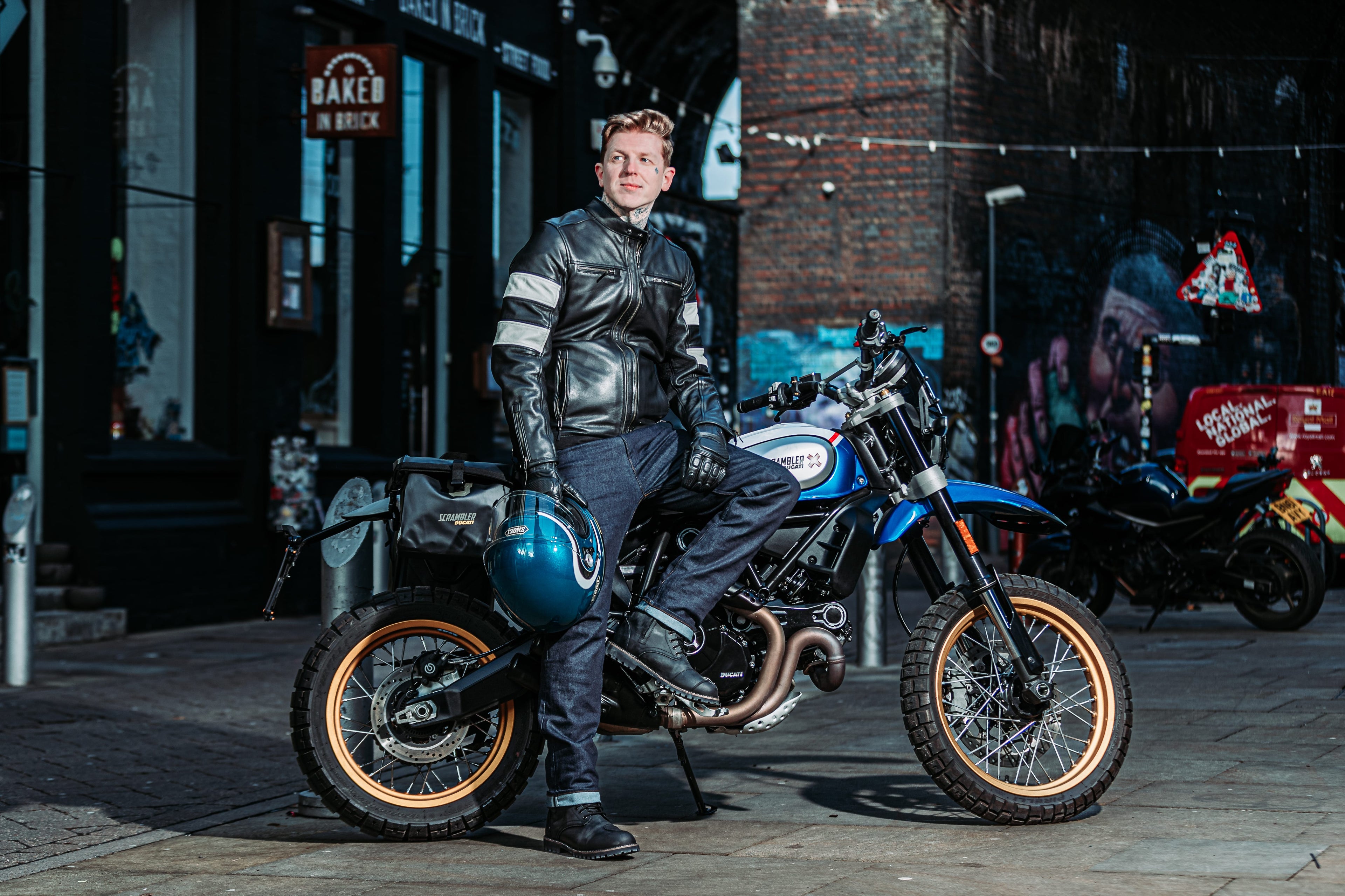 biker wearing black and ivory leather motorcycle jacket on motorbike with helmet and gear