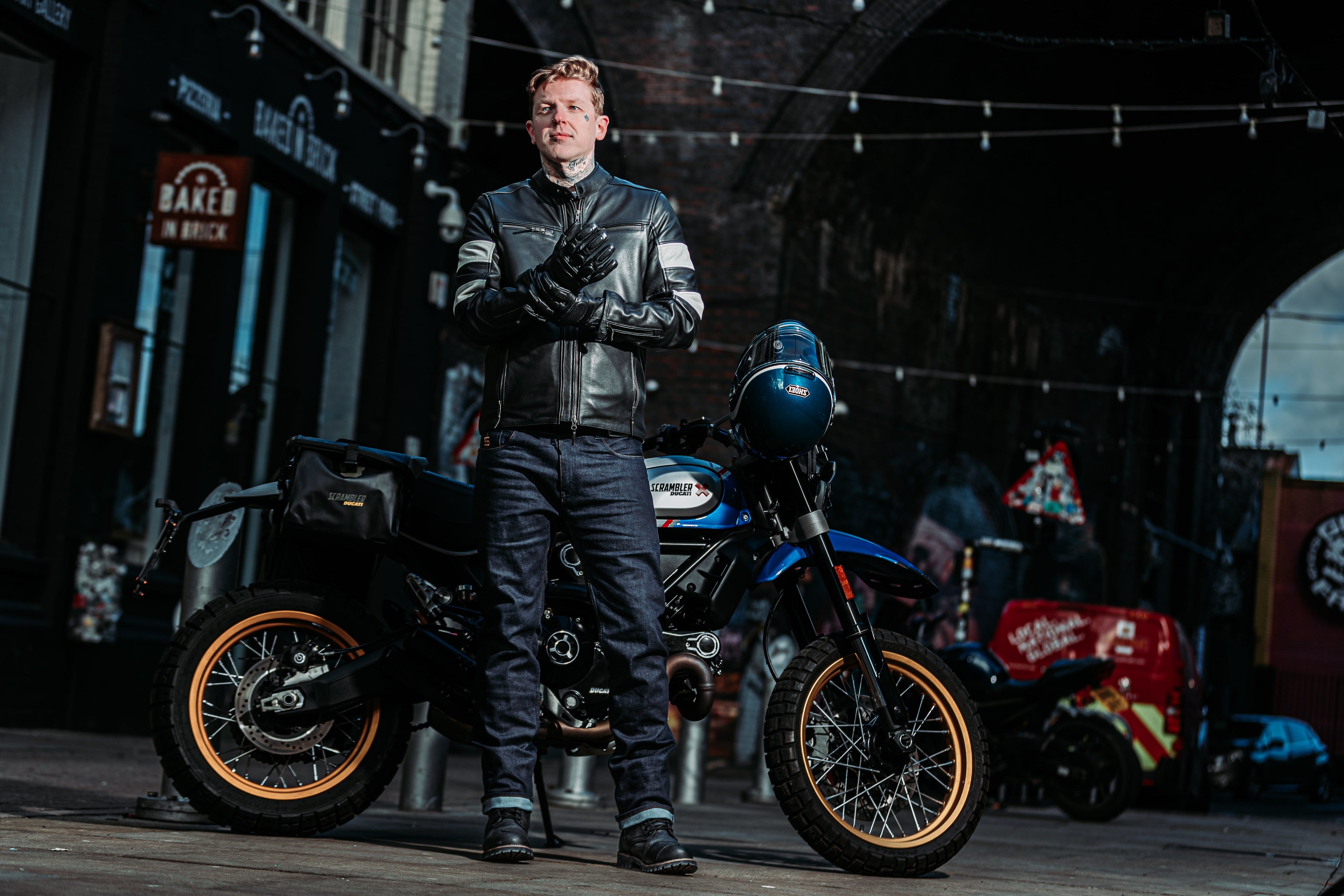 biker putting on black motorcycle gloves wearing a black leather motorcycle jacket with motorbike