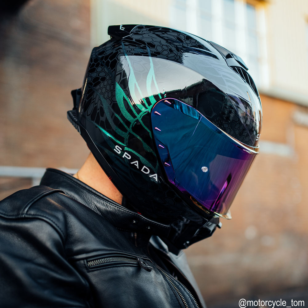 biker wearing black with green design motorcycle helmet with multicoloured visor