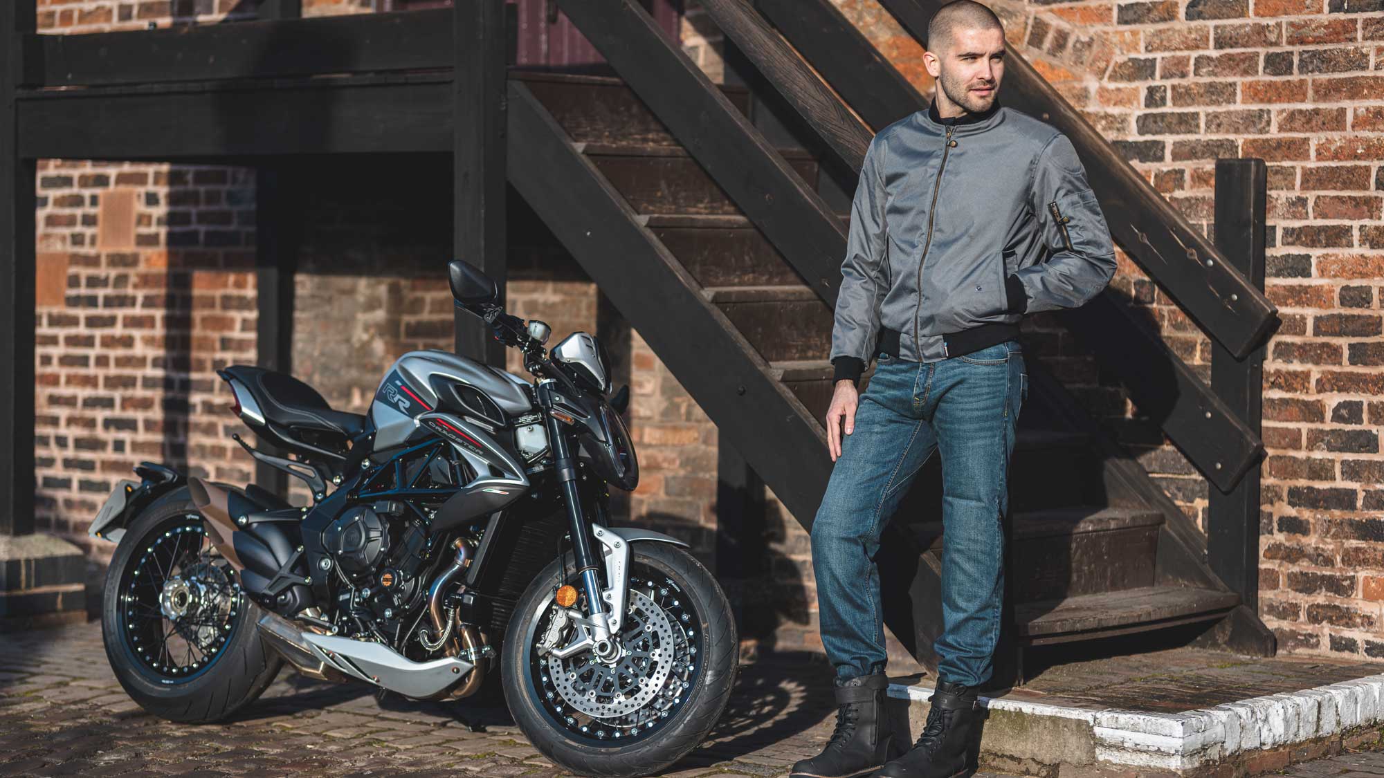 biker wearing grey bomber jacket for men with blue motorcycle jeans with motorbike