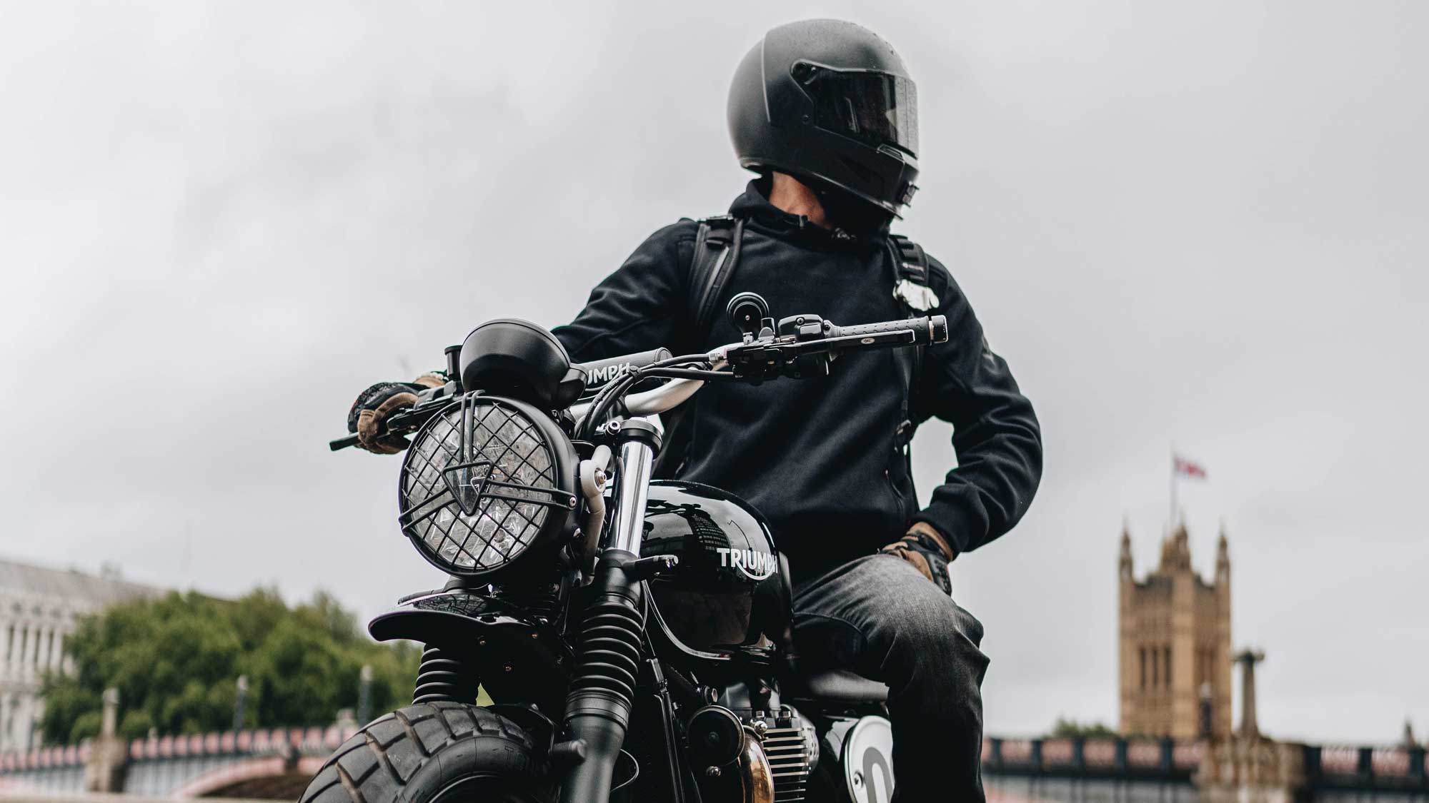 biker on triumph black motorbike with black helmet and hoodie in london