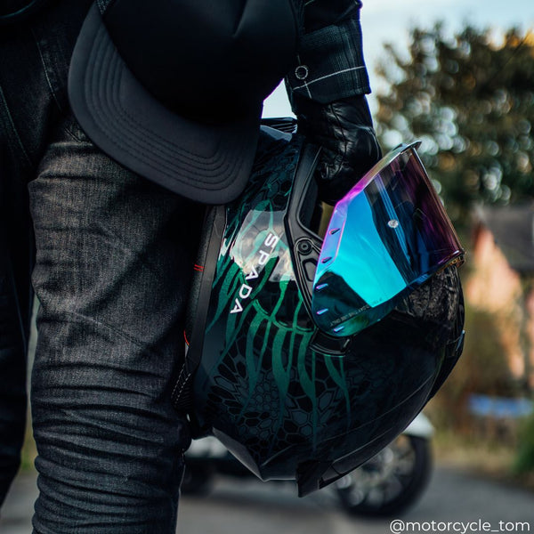 biker wearing black leather gloves holding motorbike helmet with multicolour visor