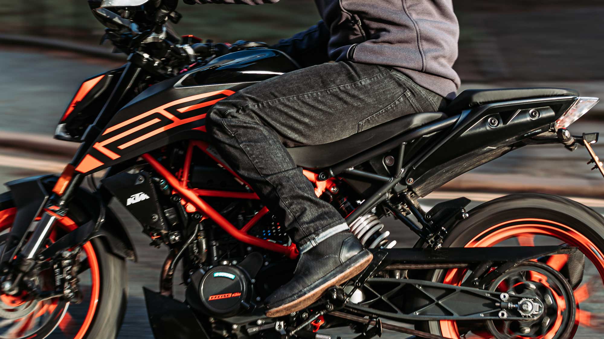 biker wearing black motorcycle jeans and black boots for men on black and orange motorbike