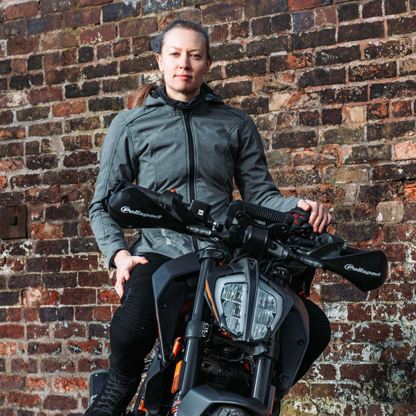 Woman sitting on black and orange motorbike wearing grey womens waterproof jacket and helmet, ready to ride in style and comfort