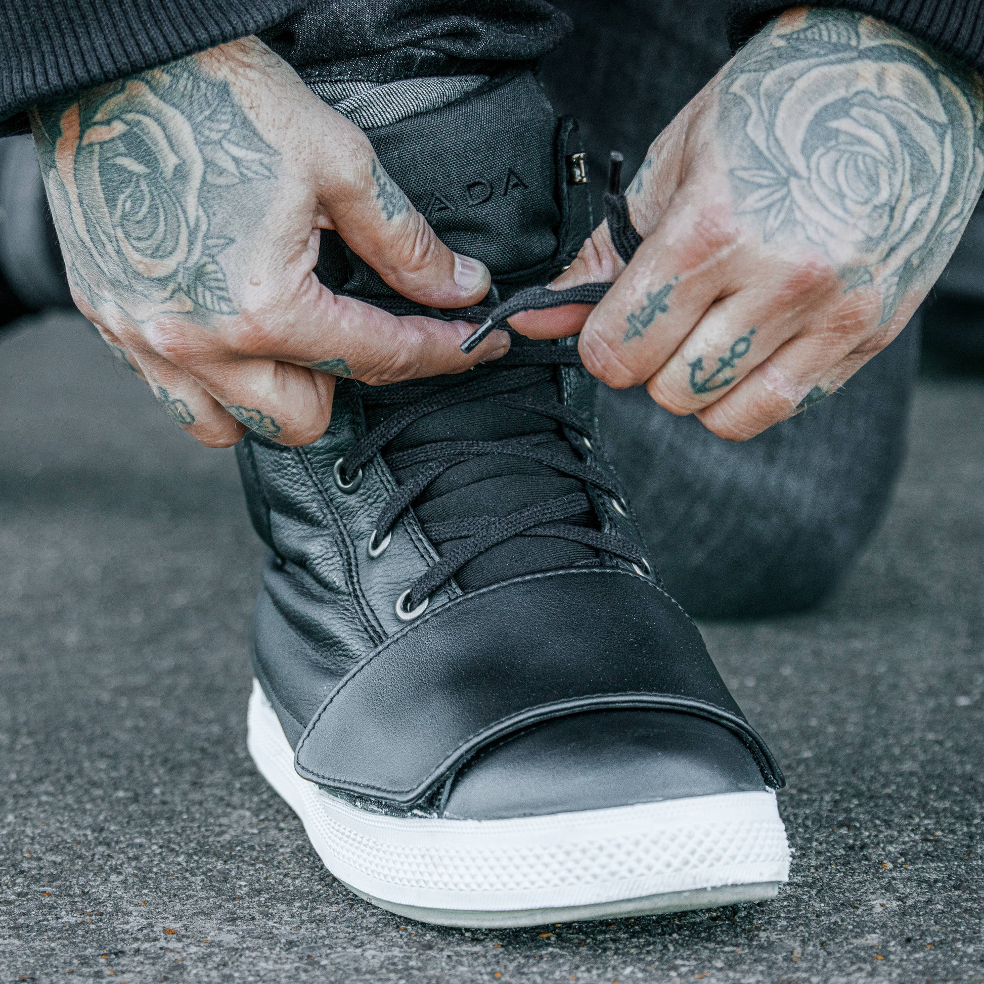 biker tying his black high top motorcycle trainers for riding