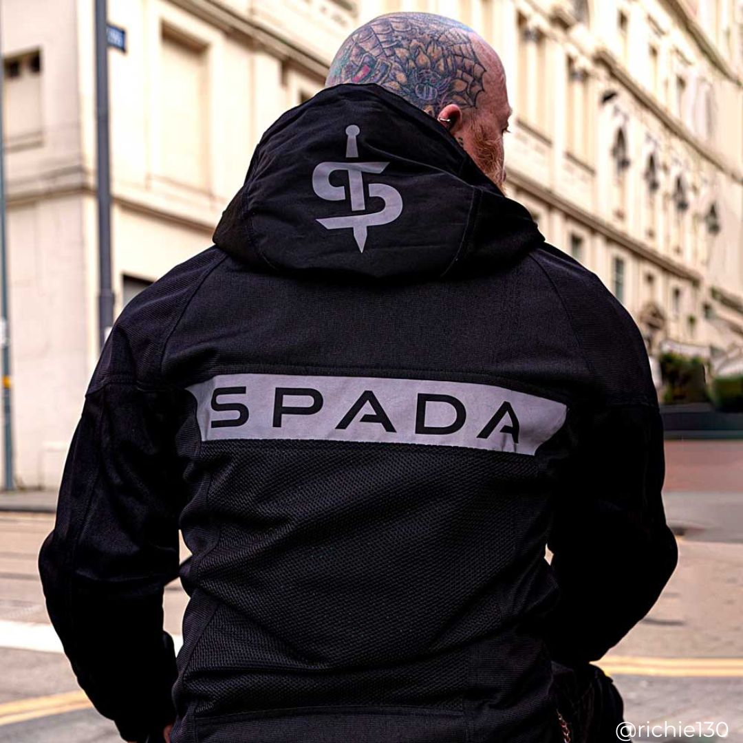 back of biker wearing black motorcycle jacket for men with reflective logos on back and hood for visibility