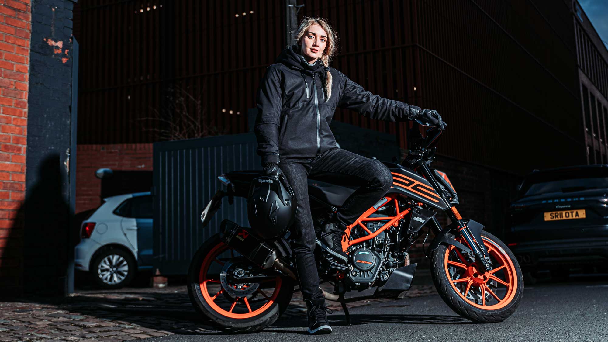 biker girl wearing black motorcycle gear including ladies motorcycle jacket on orange motorbike