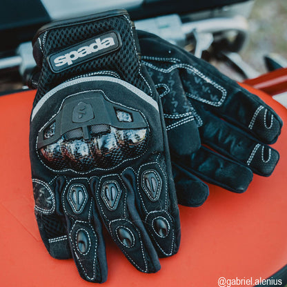 nylon black motorcycle gloves with white stitching and knuckle protection laying on a motorcycle