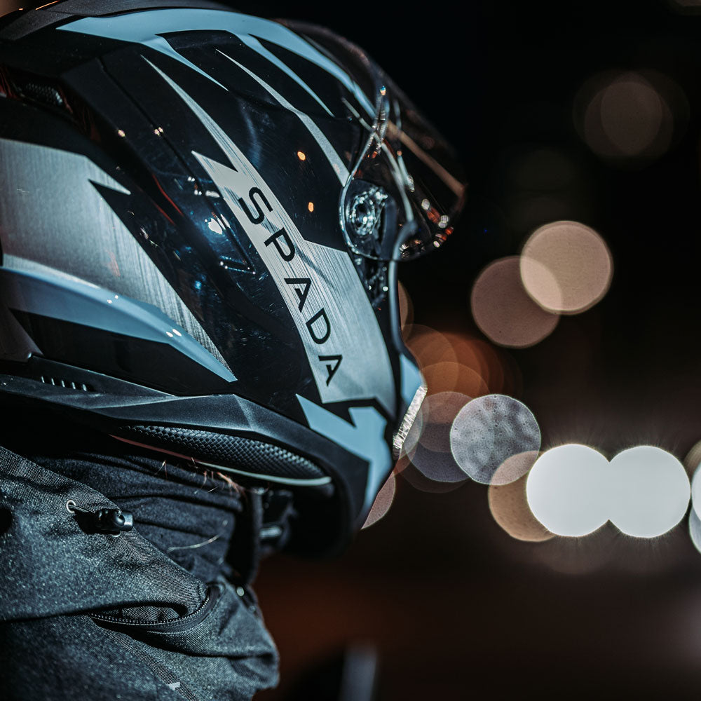 side back view of biker wearing black and grey full face motorcycle helmet with black spada logo in the night