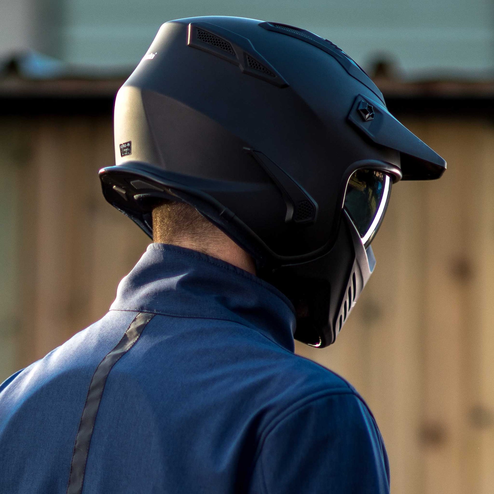 back of biker wearing blue motorbike jacket and black matte motorcycle helmet