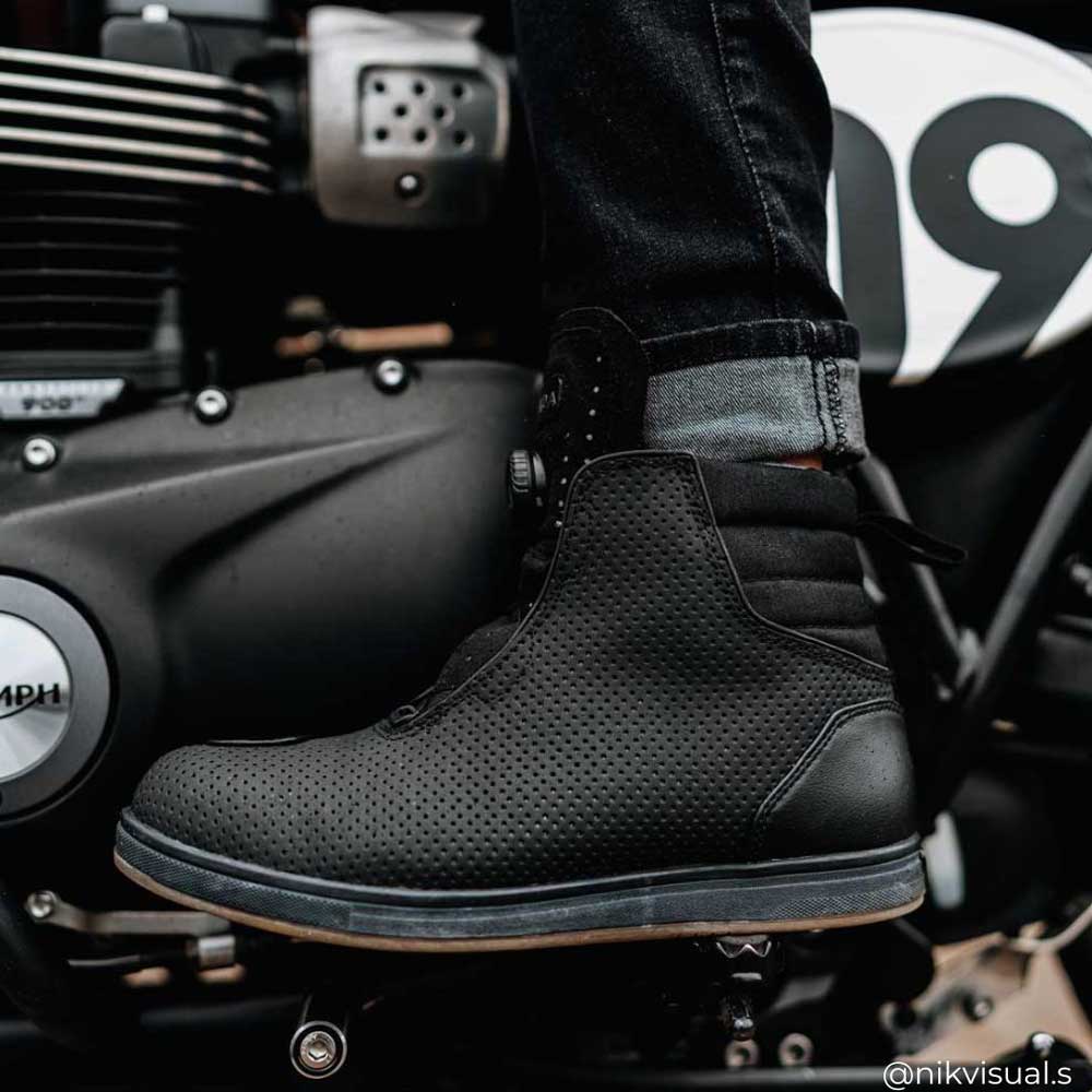 side view of black motorcycle trainers worn by biker with black motorcycle jeans on triumph bike