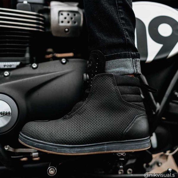 side view of black motorcycle trainers worn by biker with black motorcycle jeans on triumph bike