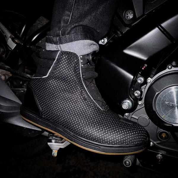 biker wearing black motorcycle boots on motorbike with reflective elements for night riding