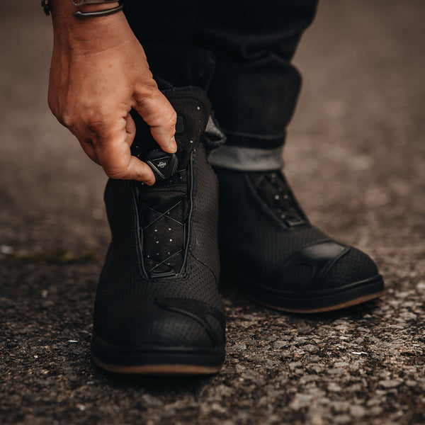 biker fastening a pair of black motorcycle reflective trainers for men