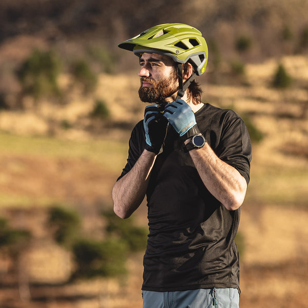 biker strapping on green mtb helmet wearing gloves and tshirt outdoors